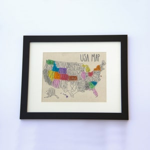 May include: A framed print of a hand-drawn map of the United States. Each state is outlined and filled with a different color, and the state name is written inside the outline. The map is titled "USA Map" in black text.