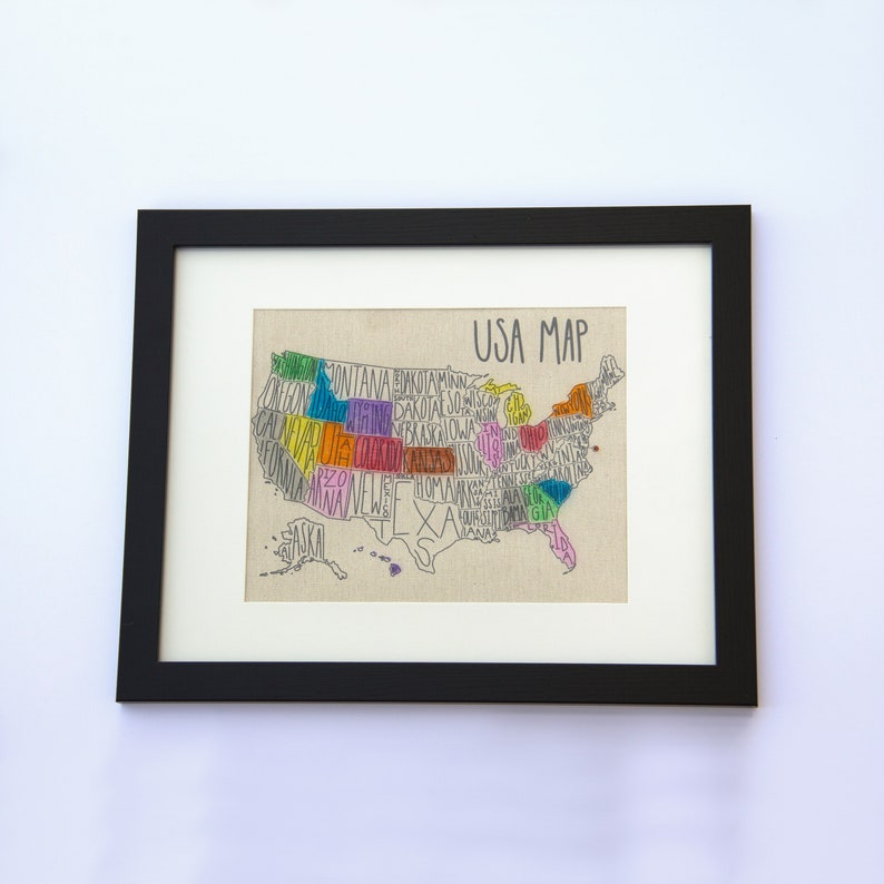 May include: A framed print of a hand-drawn map of the United States. Each state is outlined and filled with a different color, and the state name is written inside the outline. The map is titled "USA Map" in black text.