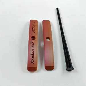 Puede incluir: Dos piezas de plástico rojo y naranja con el texto "Kraken 3D STD 5" impreso en un lado. Una herramienta de plástico negro con un extremo puntiagudo.