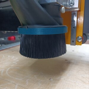 May include: A close-up of a black dust collection brush attached to a CNC machine. The brush is made of soft bristles and is designed to collect dust and debris from the work surface.