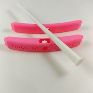 May include: Two pink plastic hoops with a white plastic rod running through them. The hoops have the text "Kraken 3D" printed on them.