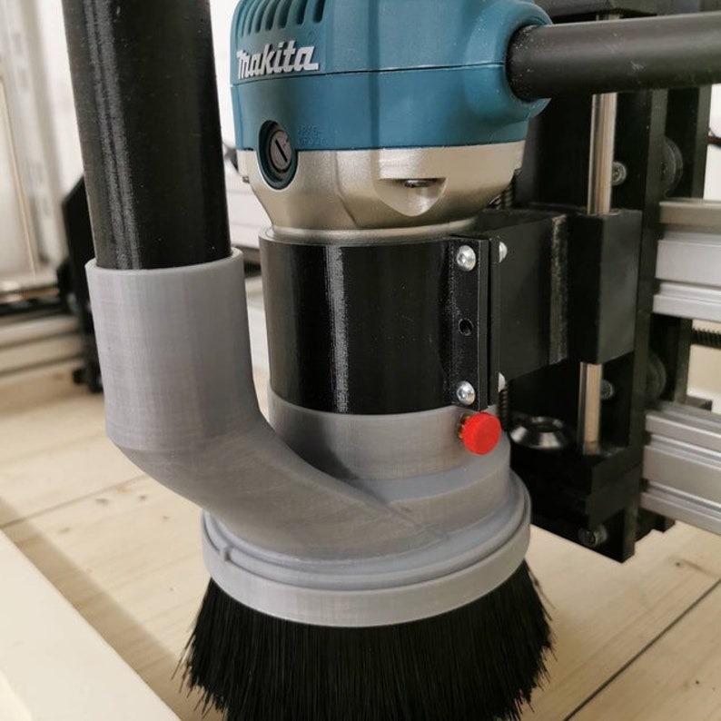 May include: A close-up of a gray and black router with a dust collection system. The router is attached to a black and silver machine. The router has a black brush and a red button.