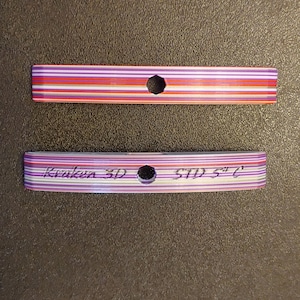 Puede incluir: Dos imágenes de primer plano de un conector de cable de computadora. La imagen superior muestra un cable multicolor con un agujero redondo en el centro. La imagen inferior muestra un cable blanco y negro con el texto "Kraken 3D STD 5"C" impreso en él.