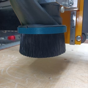 May include: A close-up of a black dust collection brush attached to a CNC machine. The brush is made of soft bristles and is designed to collect dust and debris from the work surface.