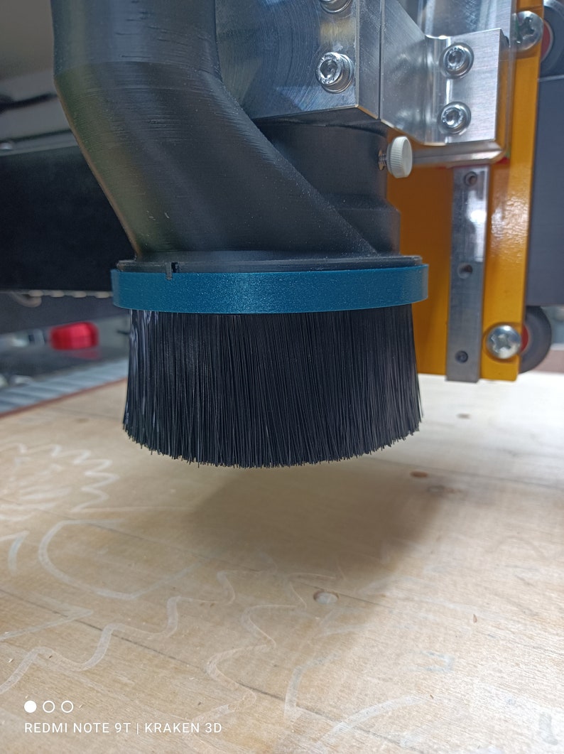 May include: A close-up of a black dust collection brush attached to a CNC machine. The brush is made of soft bristles and is designed to collect dust and debris from the work surface.