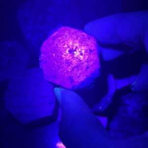 K&ouml;nnte beinhalten: Nahaufnahme eines gro&szlig;en, facettierten, violetten Edelsteins unter UV-Licht. Der Edelstein ist tiefviolett und hat ein sternf&ouml;rmiges Muster in der Mitte.