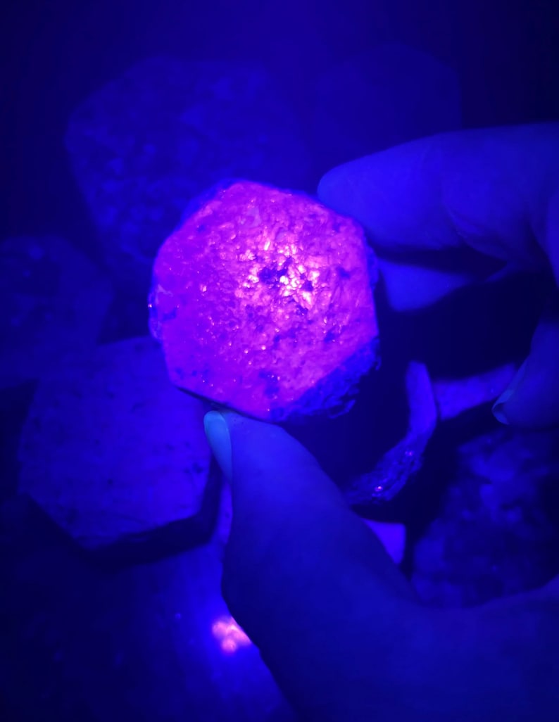 K&ouml;nnte beinhalten: Nahaufnahme eines gro&szlig;en, facettierten, violetten Edelsteins unter UV-Licht. Der Edelstein ist tiefviolett und hat ein sternf&ouml;rmiges Muster in der Mitte.