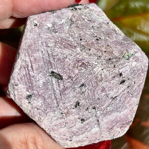 K&ouml;nnte beinhalten: Ein gro&szlig;er, rauer, rosafarbener Rubin-Kristall mit sechseckiger Form. Der Kristall hat eine gestreifte Oberfl&auml;che und ist mit kleinen schwarzen Einschl&uuml;ssen bedeckt.