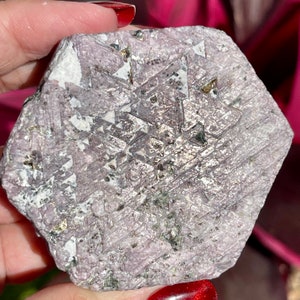 K&ouml;nnte beinhalten: Ein gro&szlig;er, rauer, sechseckiger, purpurgrauer Edelstein mit einem geometrischen Muster aus kleineren Kristallen und goldenen Flocken.