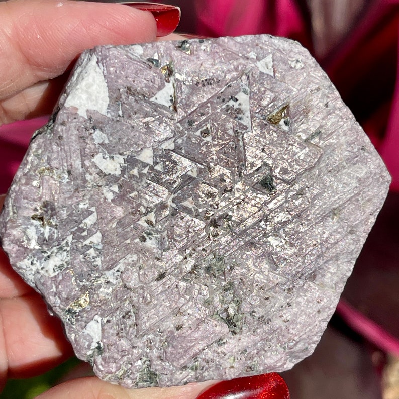 K&ouml;nnte beinhalten: Ein gro&szlig;er, rauer, sechseckiger, purpurgrauer Edelstein mit einem geometrischen Muster aus kleineren Kristallen und goldenen Flocken.
