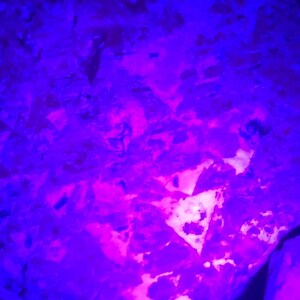 K&ouml;nnte beinhalten: Ein gro&szlig;er, unregelm&auml;&szlig;ig geformter Stein, der mit einem leuchtend violetten Licht beleuchtet wird. Der Stein hat eine raue, strukturierte Oberfl&auml;che und scheint aus Salzkristallen zu bestehen.