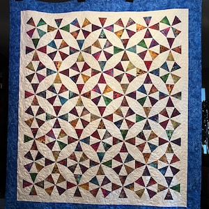 May include: A colorful quilt with a geometric pattern of triangles and circles. The quilt is made with a variety of fabrics in shades of purple, green, brown, and white. The quilt is edged with a blue border.