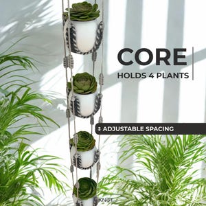 May include: A vertical hanging planter featuring four white pots held by grey and beige macrame cord, each containing a green succulent. Text on the image reads: CORE HOLDS 4 PLANTS and ADJUSTABLE SPACING. The design allows for vertical plant display.