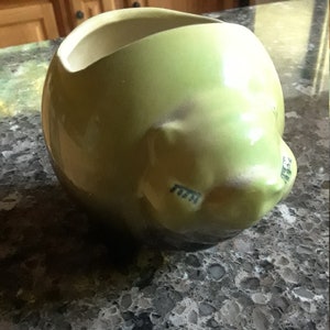 May include: A green ceramic planter shaped like a sleeping cat. The planter has a glazed finish and a small opening at the top for planting.