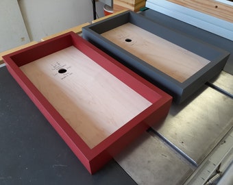 May include: Two wooden trays with a hole in the center. One tray is painted red and the other is painted gray. The trays are sitting on a metal surface.