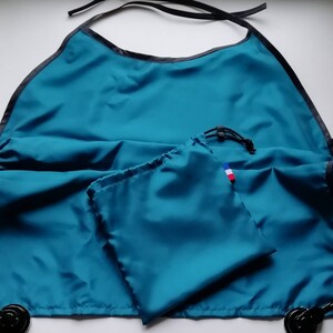 Peut inclure: Un tablier imperméable bleu sarcelle avec une bordure noire et un sac à cordon assorti bleu sarcelle. Le sac a un petit drapeau français cousu dessus.