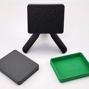 May include: A black, textured, square tripod with three legs, a matching square base, and a green square tray with the text "Yalotz Creations". The items are displayed on a white surface.