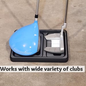May include: A golf club holder with a blue driver and a silver putter. The clubs are resting in a black tray. The text "Works with wide variety of clubs" is displayed at the bottom.