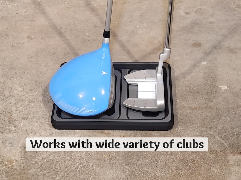 May include: A golf club holder with a blue driver and a silver putter. The clubs are resting in a black tray. The text "Works with wide variety of clubs" is displayed at the bottom.