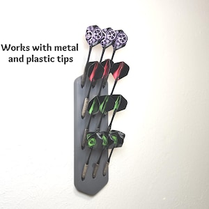May include: A grey wall-mounted dart holder displaying nine darts with various colored flights and shafts. The text "Works with metal and plastic tips" is printed to the left of the holder. The darts feature purple, red, and green patterned flights.