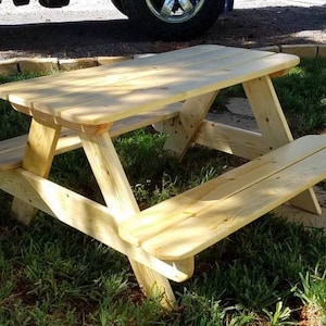 Può includere: Un piccolo tavolo da picnic in legno con finitura in legno naturale. Il tavolo ha un piano rettangolare e due panche.