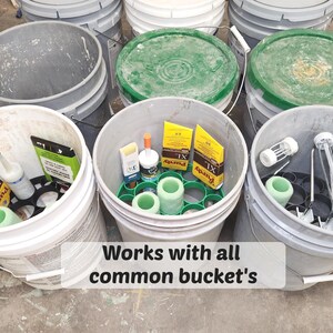 May include: A collection of gray and white buckets filled with various supplies. Some buckets contain green and white items, while others hold yellow boxes and cylindrical objects. The text "Works with all common bucket's" is visible.