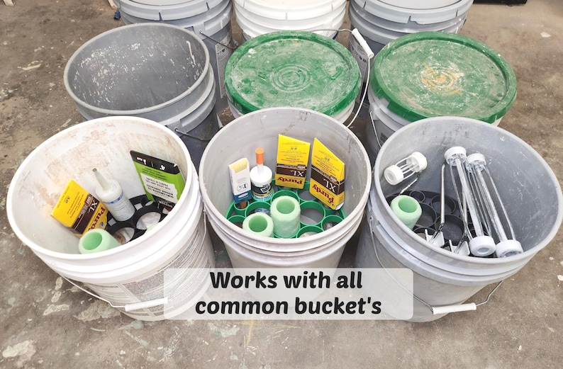 May include: A collection of gray and white buckets filled with various supplies. Some buckets contain green and white items, while others hold yellow boxes and cylindrical objects. The text "Works with all common bucket's" is visible.