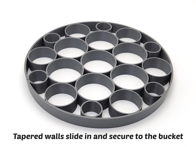 May include: A gray, circular object with multiple cylindrical openings. The text "Tapered walls slide in and secure to the bucket" is visible at the bottom of the image. The object appears to be made of plastic or a similar material.