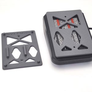 May include: A gray 3D-printed device with a rectangular base and a matching lid featuring geometric cutouts. The device is connected to a black cable. The lid has the text "Yalotz Creations".