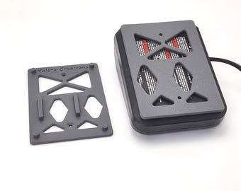 May include: A grey rectangular plastic mounting plate with the text Yalotz Creations printed on it, featuring geometric cutouts and four small circular feet. Next to it is a black electronic device with a matching grey plate attached to its base.