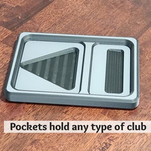 May include: A gray rectangular organizer with three compartments. The organizer has a light gray interior and a dark gray border. The text "Pockets hold any type of club" is printed on the bottom. The organizer is on a wooden surface.