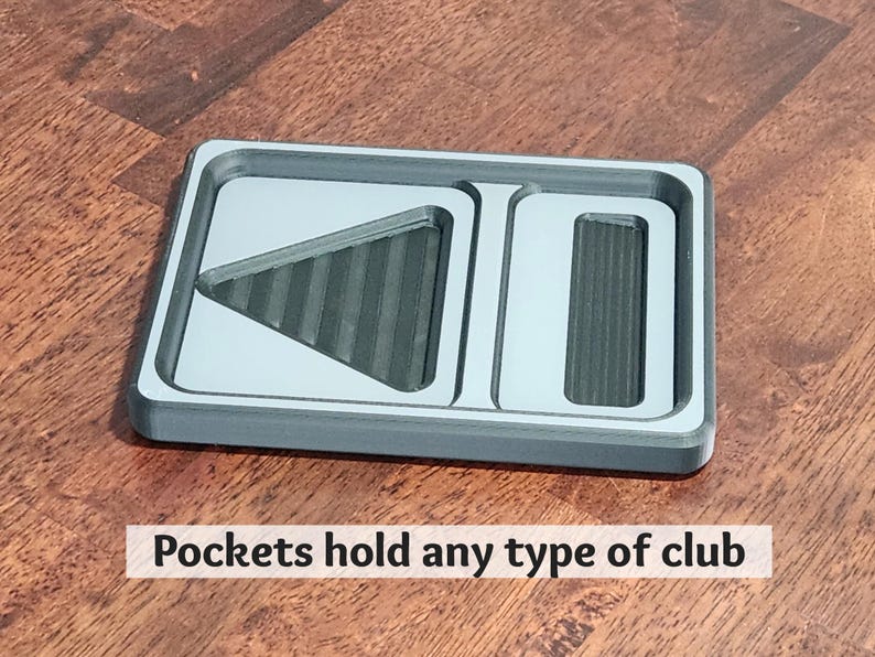 May include: A gray rectangular organizer with three compartments. The organizer has a light gray interior and a dark gray border. The text "Pockets hold any type of club" is printed on the bottom. The organizer is on a wooden surface.