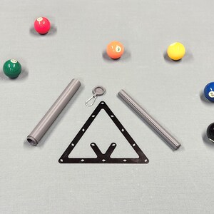 May include: A black triangular billiard rack, two grey cylindrical metal tubes, a small silver carabiner with a circular attachment, and seven colorful billiard balls including red, green, orange, yellow, blue, and black numbered spheres.