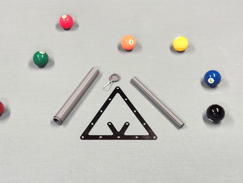 May include: A black triangular billiard rack, two grey cylindrical metal tubes, a small silver carabiner with a circular attachment, and seven colorful billiard balls including red, green, orange, yellow, blue, and black numbered spheres.