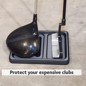May include: A black and gray golf club holder with a driver and putter. The holder has two compartments and the text "Protect your expensive clubs". The driver is black with a textured face.