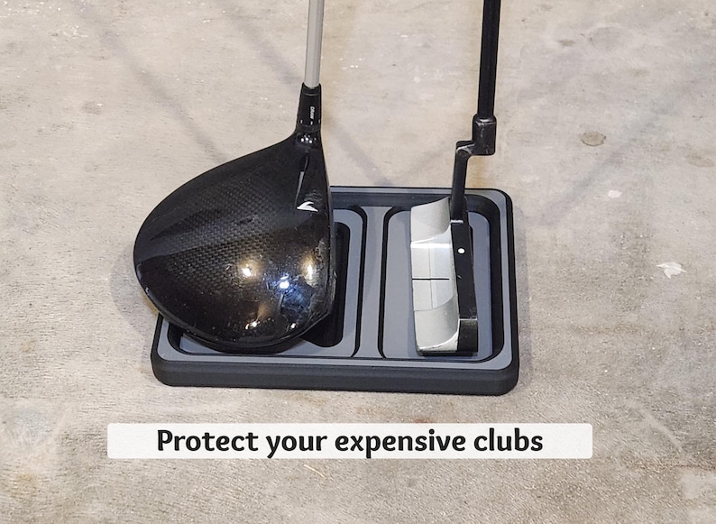 May include: A black and gray golf club holder with a driver and putter. The holder has two compartments and the text "Protect your expensive clubs". The driver is black with a textured face.