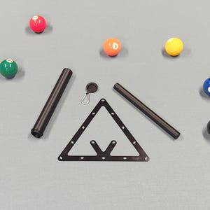 May include: A black triangular billiard rack, two black cylindrical tubes, and a small black circular keychain with a silver carabiner clip. Six colorful numbered billiard balls in red, green, orange, yellow, blue, and black are scattered around.