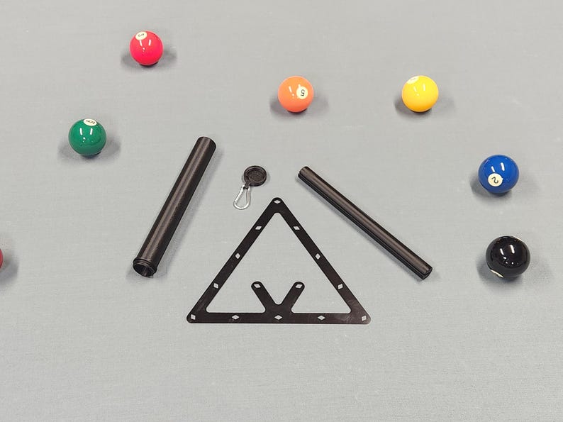 May include: A black triangular billiard rack, two black cylindrical tubes, and a small black circular keychain with a silver carabiner clip. Six colorful numbered billiard balls in red, green, orange, yellow, blue, and black are scattered around.
