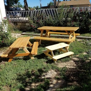 May include: Three wooden picnic tables in a grassy backyard. The largest table is in the center, with two smaller tables to the left and right. All tables are made of natural wood and have a rustic look.