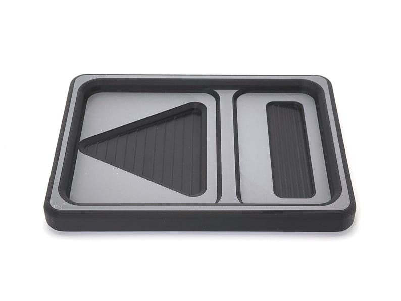 May include: A rectangular black and silver tray with three distinct sections. The tray has a raised edge and a silver interior. Two sections have a ridged, dark gray surface.