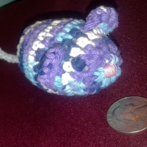 May include: A crocheted purple, blue, and white cat toy shaped like a mouse. The toy has a pink nose and a white tail.