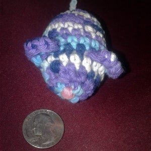 May include: A crocheted stuffed animal shaped like a pig. The pig is purple, blue, and white with a pink nose.