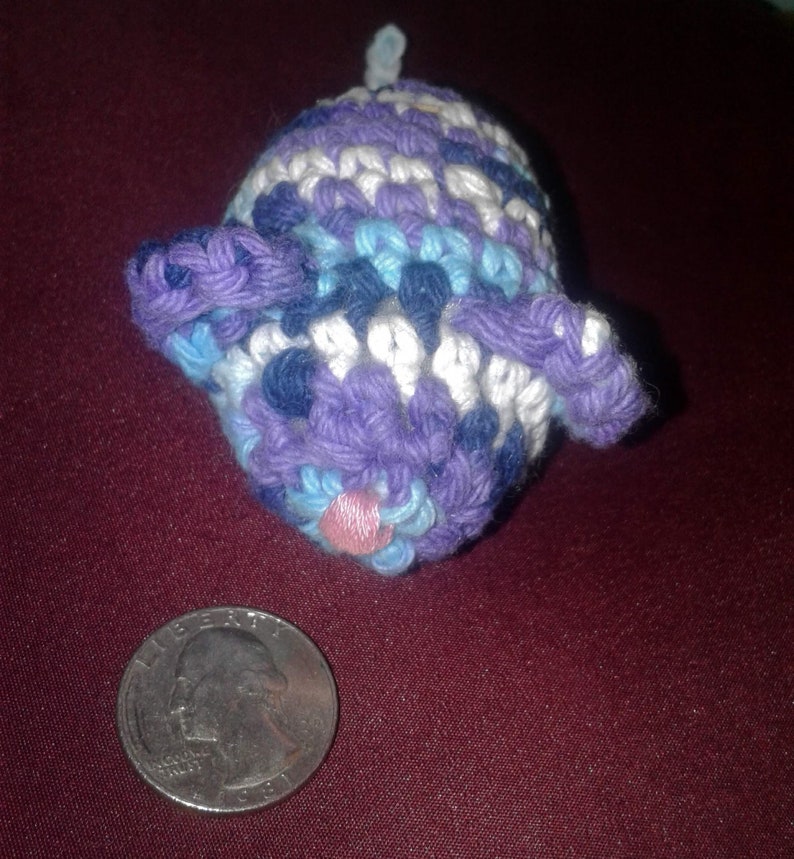 May include: A crocheted stuffed animal shaped like a pig. The pig is purple, blue, and white with a pink nose.