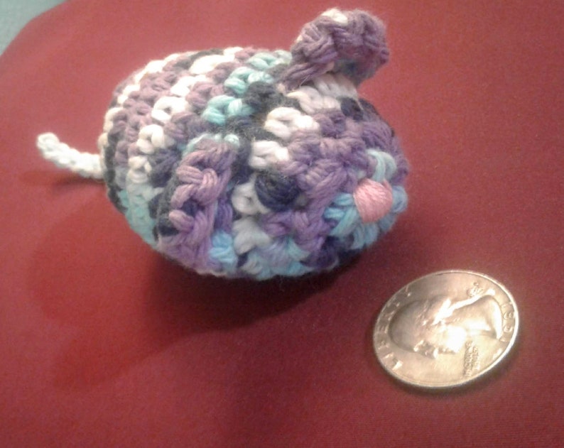 May include: A crocheted mouse toy with a purple, blue, and white color scheme. The mouse has a pink nose and a long tail.