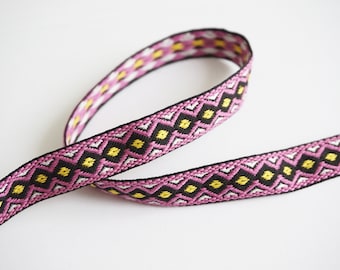 May include: Pink, black, white, and yellow woven trim with a geometric pattern.