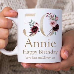 May include: White ceramic mug with a gold 50 and floral design. The text "Annie Happy Birthday Love Lisa and Simon xx" is printed on the mug.