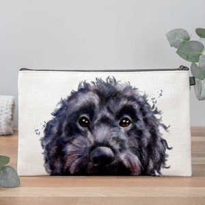 May include: A white canvas makeup bag with a black zipper and a watercolour illustration of a black dog's face. The dog is looking directly at the viewer.