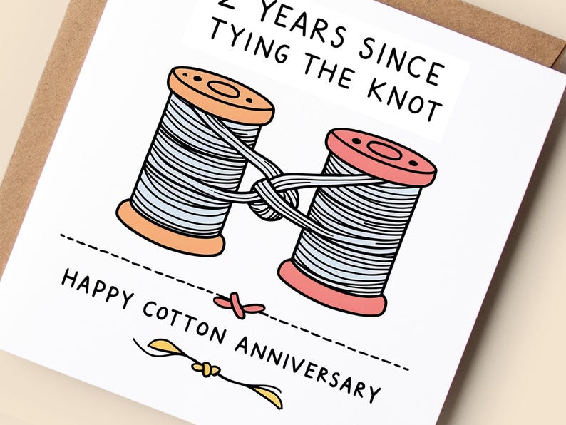 May include: A square greeting card featuring a cartoon illustration of two wooden spools of light blue thread tied together. The text reads 2 YEARS SINCE TYING THE KNOT and HAPPY COTTON ANNIVERSARY. The card is white with black line art and text.