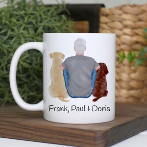 K&ouml;nnte beinhalten: Wei&szlig;e Keramiktasse mit einem Design einer Person und zwei Hunden, einem gelben Labrador und einem braunen Hund. Auf der Tasse stehen die Namen "Frank, Paul & Doris". Die Tasse hat einen wei&szlig;en Henkel.