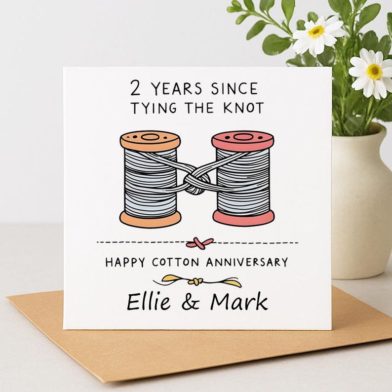May include: A square greeting card with white background featuring two spools of thread tied together with a knot. Text reads: 2 YEARS SINCE TYING THE KNOT, HAPPY COTTON ANNIVERSARY, and Ellie & Mark. The illustration uses orange, pink, and grey colors.
